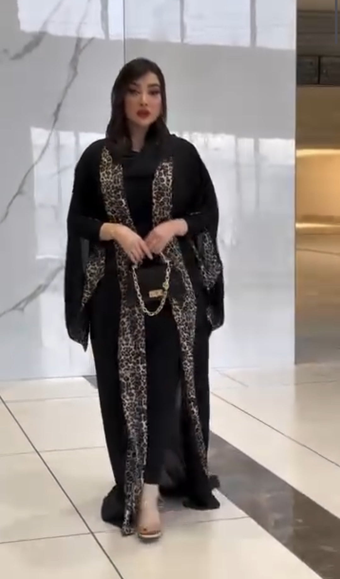 Woman in a black abaya with gold embroidery standing in a modern indoor setting.