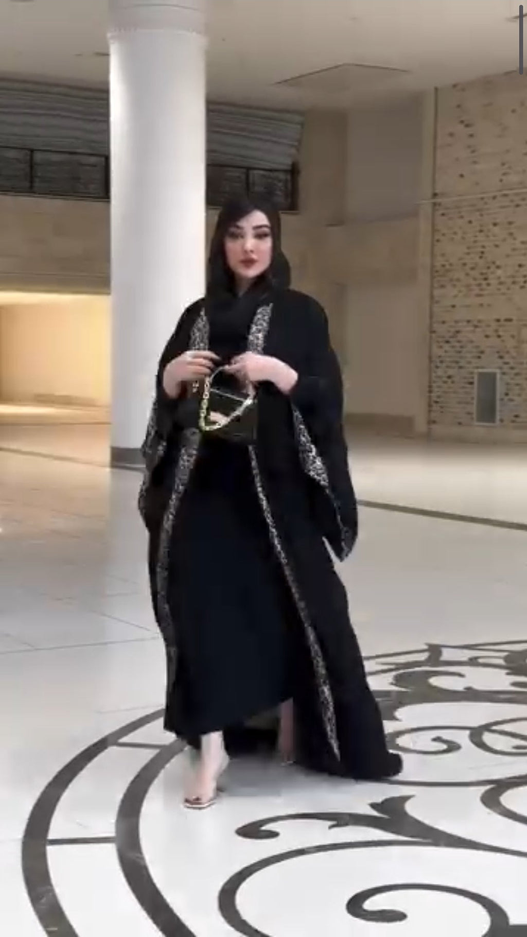 Woman in a black abaya standing in a modern indoor setting with decorative floor.