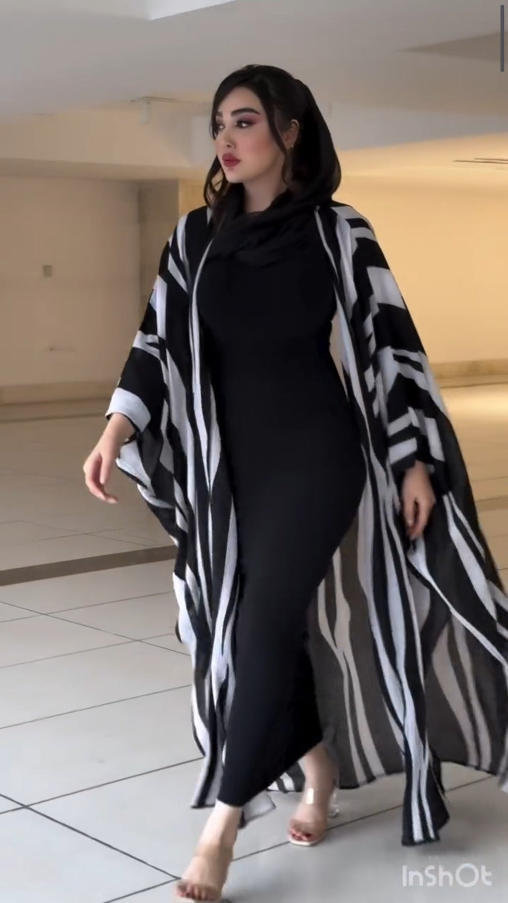 Woman wearing a black and white patterned kimono over a black outfit in an indoor setting.