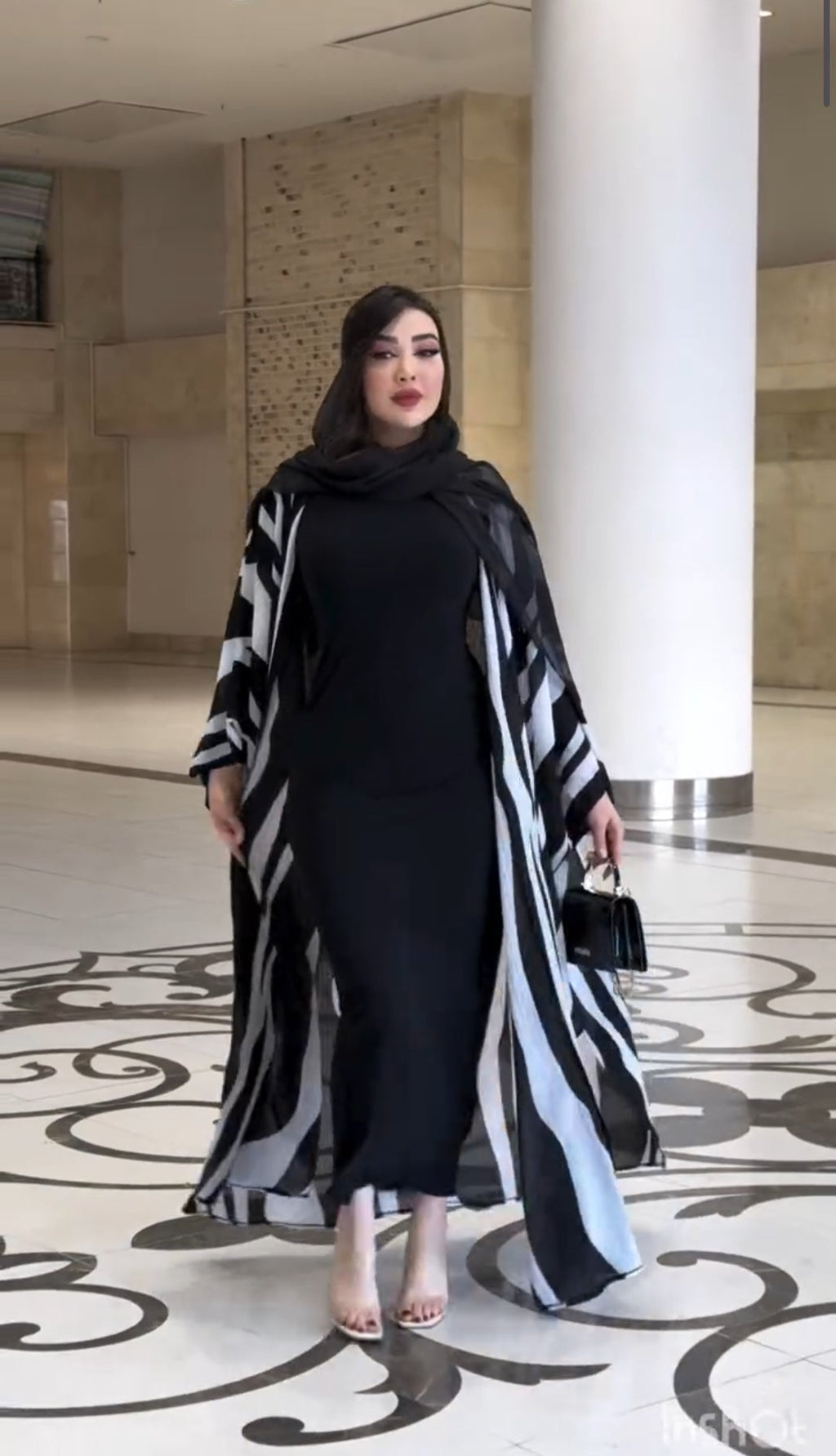 Woman in a black and white striped outfit standing in a modern indoor setting with columns.