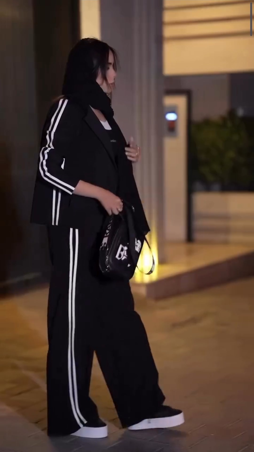Person wearing a black tracksuit with white stripes outdoors at night.